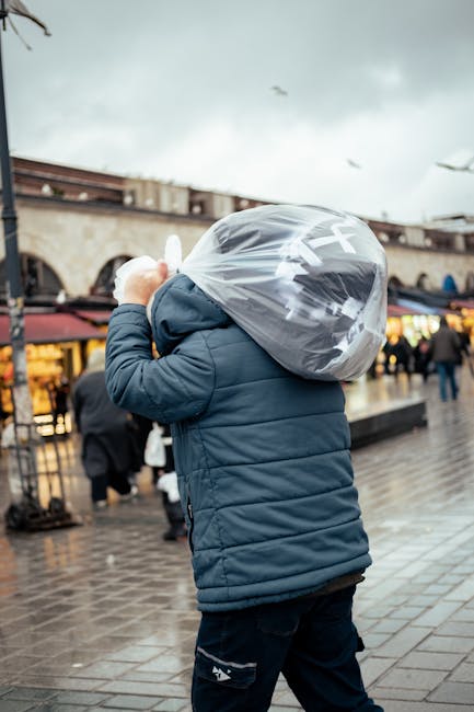 A bustling outdoor market street with narrow cobblestone pathways, lined on both sides by various stalls and shops displaying clothing, accessories, and mannequins dressed in fashionable garments. On